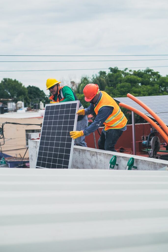 Two workers in safety gear installing solar panels on a rooftop for sustainable energy.